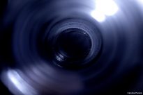 Fotografia vertical do interior de um pote de vidro azul, visto de cima. Uma luz entra pela borda superior e cria um reflexo brilhante com o fundo em tom escuro.