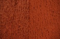Fotografia horizontal de uma quina de parede chapiscada, em tons de vermelho e textura irregular.